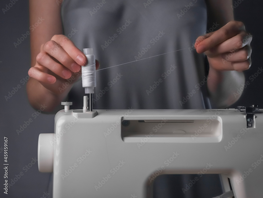Fototapeta premium Seamstress hands putting thread spool on sewing machine close up.