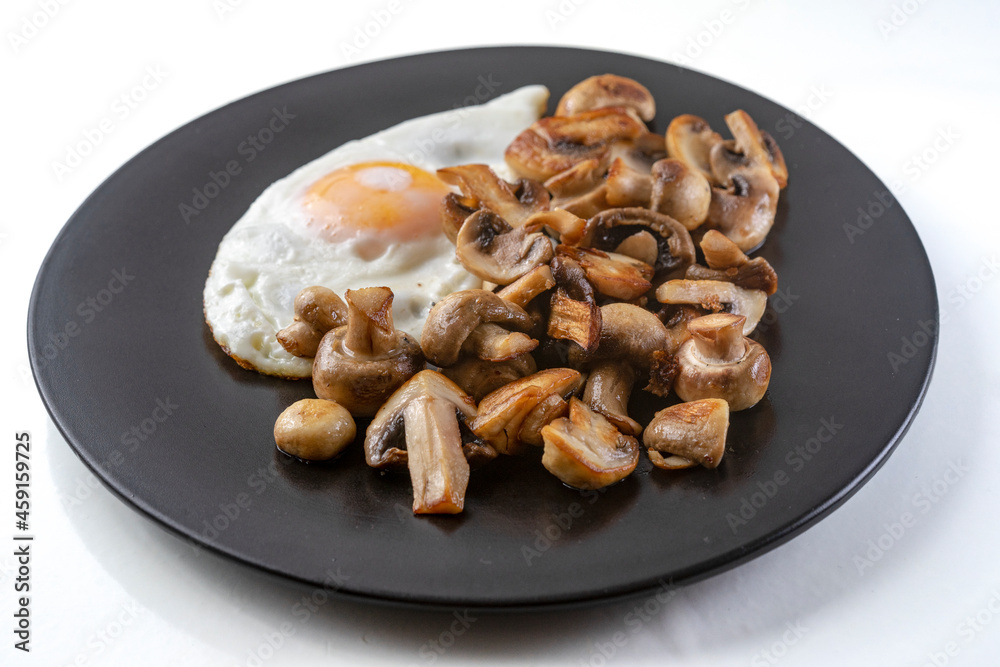 Fried champignon mushrooms with a fried egg on a black plate, isolated on white background Fried champignon mushrooms with a fried egg on a black plate, isolated on white background