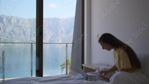 Wallpaper Mural Girl making a video call with a laptop, sitting in her bed view a nice sea view.  Torontodigital.ca