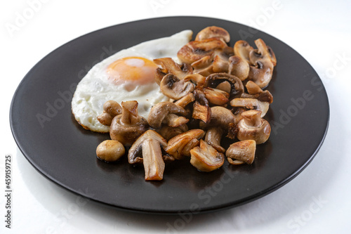 Fried champignon mushrooms with a fried egg on a black plate, isolated on white background