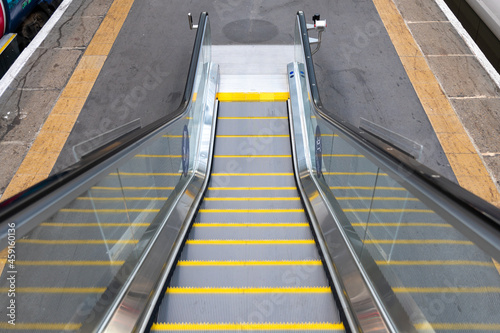 Escalator with yellow edged steps going down onto a railway station platform