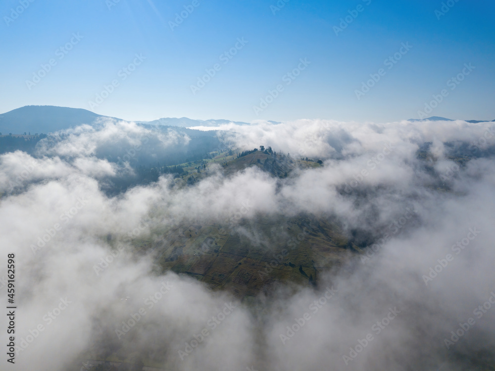 A thin morning fog covers the Ukrainian mountains. Green grass on the slopes of the mountains. A curly thin fog spreads over the mountains. Aerial drone view.