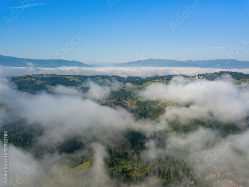 A thin morning fog covers the Ukrainian mountains. Green grass on the slopes of the mountains. A curly thin fog spreads over the mountains. Aerial drone view.