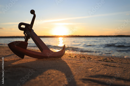 Fototapeta Wooden anchor on shore near river at sunset