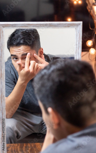 Hispanic teenager checking acne in a mirror in the living room. Appearance in adolescence concept.