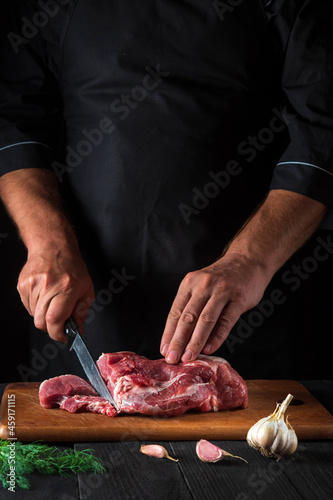 The chef cuts meat with a knife in the kitchen prepares food. Vegetables and spices on the kitchen table in a restaurant to prepare a delicious lunch
