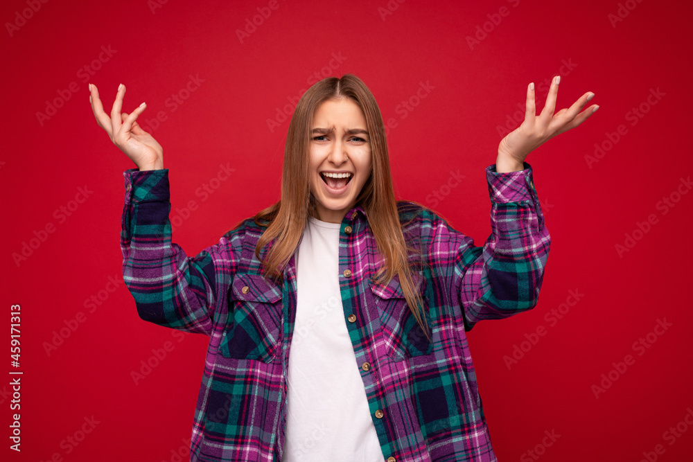 Portrait of young emotional asking dissatisfied attractive dark blonde woman with sincere emotions wearing hipster purple check shirt and white t-shirt with empty space isolated over red background Portrait of young emotional asking dissatisfied attractive dark blonde woman with sincere emotions wearing hipster purple check shirt and white t-shirt with empty space isolated over red background