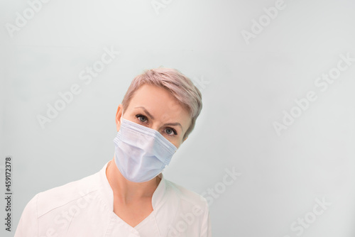 A female doctor in a medical mask looks attentively at the camera. Place for your text. Concept