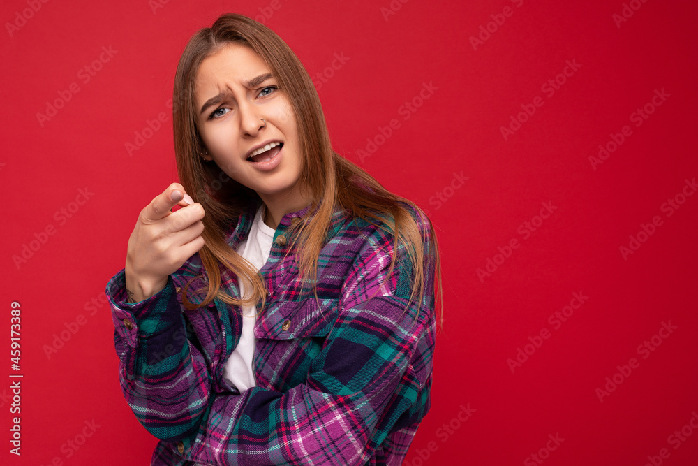 Photo of dissatisfied offended sad young beautiful dark blonde woman with sincere emotions wearing hipster purple check shirt isolated over red background with copy space and pointing finger at you Photo of dissatisfied offended sad young beautiful dark blonde woman with sincere emotions wearing hipster purple check shirt isolated over red background with copy space and pointing finger at you