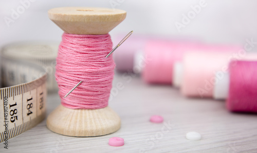 Canvas Print A spool of pink thread, a cloth and a needle on a wooden table