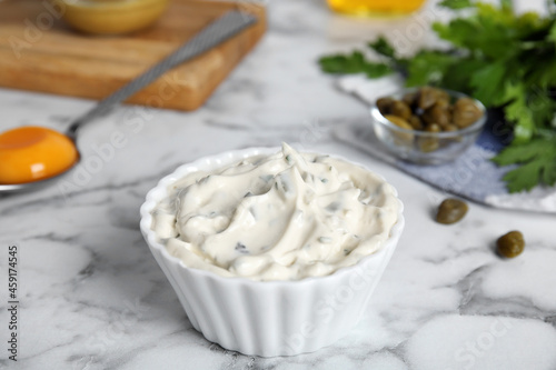 Tasty tartar sauce and ingredients on white marble table