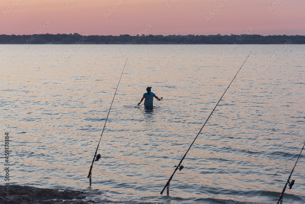 Asian man wade fishing spin casting near row of poles at Lavon Lake near Dallas, Texas, USA Asian man wade fishing spin casting near row of poles at Lavon Lake near Dallas, Texas, USA