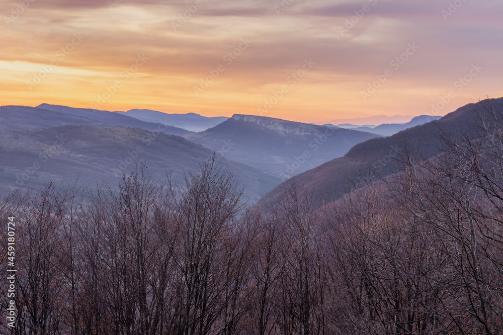 Soft sunrise view of distant rocky summit raising above the valley, dramatic, colorful sky and foreground forest