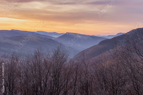 Soft sunrise view of distant rocky summit raising above the valley, dramatic, colorful sky and foreground forest