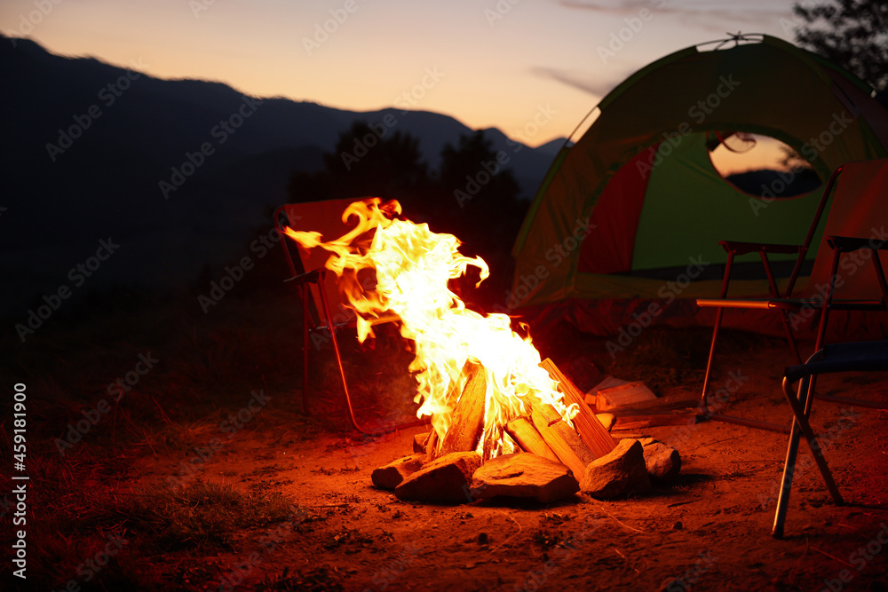 Beautiful bonfire and folding chairs near camping tent outdoors in evening