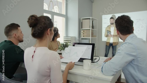 Group of young people in smart casual wear analyzing data on projection screen