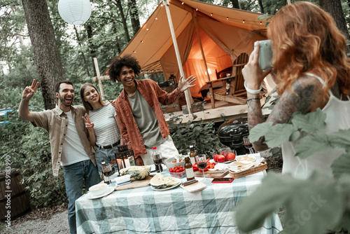 Red-haired young woman making polaroid photo of her friends on picnic, camping glamping life, resting with diverse friends outdoors, enjoying summer camping trip, having fun time in forest, copy space