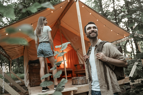 Romantic couple camping outdoors and standing in glamping tent. Happy Man and woman on a romantic camping vacation. Man with backpack with his girlfriend millennials arrived at glamping site.