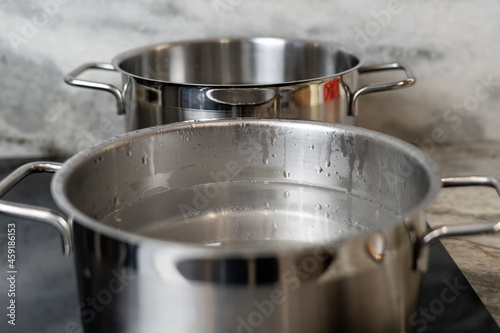 Stainless steel pots filled with water on black ceramic hob and marble countertop