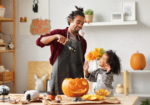Photos Ethnic father removing pulp from ripe pumpkin while carving jack o lantern with