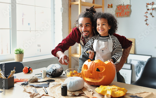 Slika na platnu Ethnic father removing pulp from ripe pumpkin while carving jack o lantern with