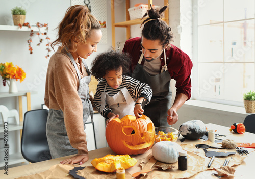Картината върху платно Happy african american family mother, father and child son carving pumpkin for H
