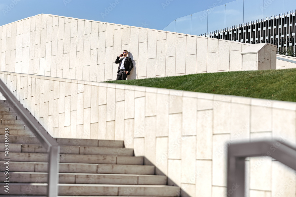 Young businessman speaking on mobile phone smartphone while standing on concrete stairs outside