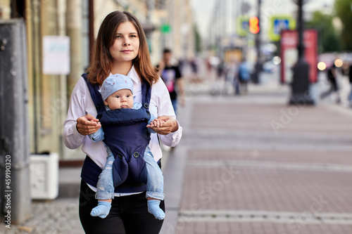 Woman walks with baby in sling on crowded street. © grigvovan