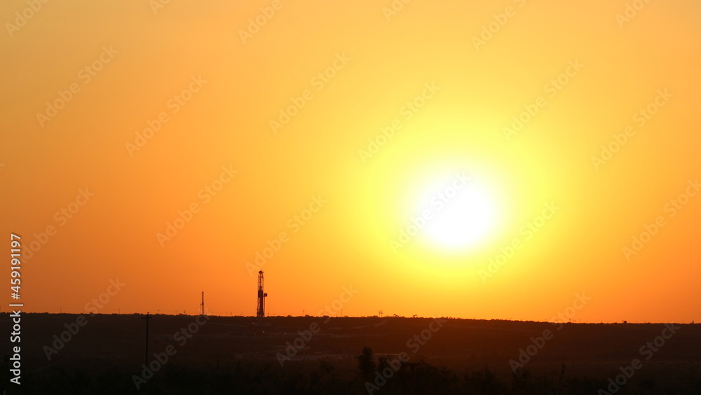 Fototapeta premium Two drilling rigs peak over the horizon with a firing red sunset view across the skyline in West Texas Permian Basin