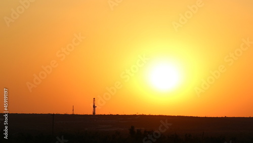 Two drilling rigs peak over the horizon with a firing red sunset view across the skyline in West Texas Permian Basin