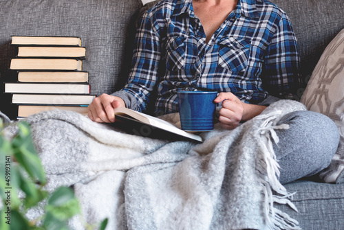 Woman sitting on couch reading book and drinking coffee or tea