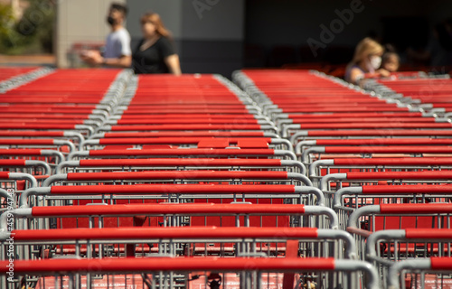 Bild auf Leinwand A row of red shopping carts with people wearing masks diffused in the background