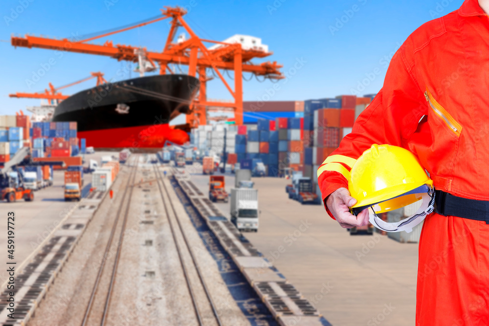 Dock worker holding hard hat for controlling work process container ship being unloaded with  in the harbor