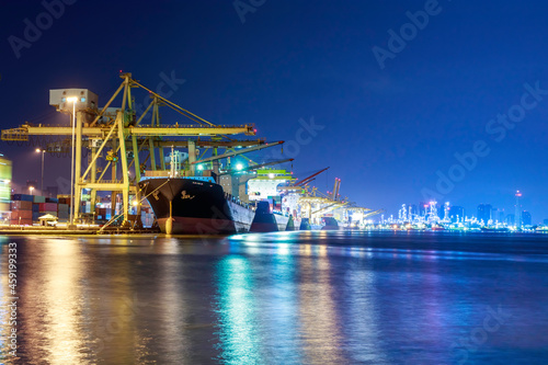 Container cargo ship with ports crane bridge in harbor and refinery industrial at night logistics and transportation concept photo