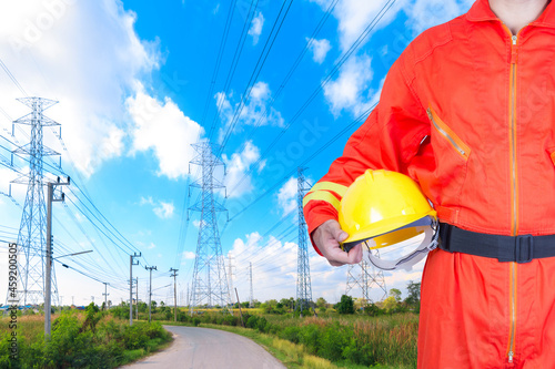 Engineer holding hard hat for working at high voltage power pylon against blue sky