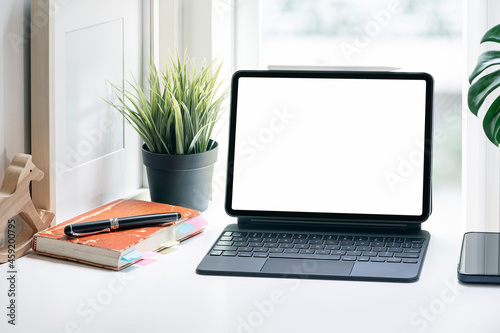 Blank screen tablet with magic keyboard on white table in living room, home office concept.
