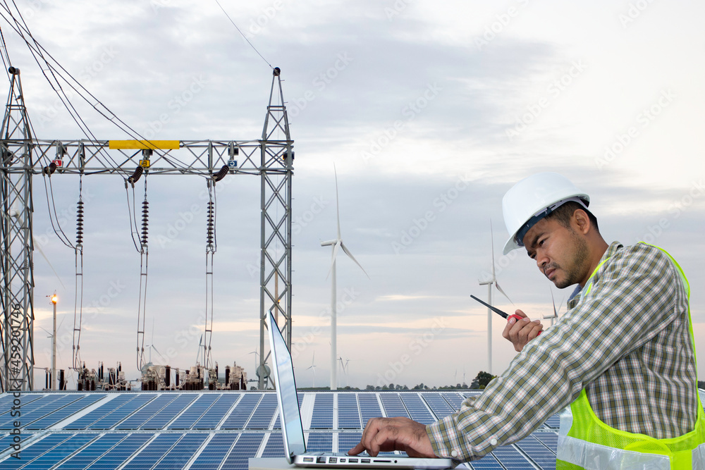 Engineer looking at tablet computer during working at solar cell panel on the rooftop against wind turbine power plant