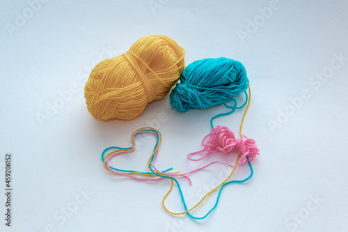 Green, yellow and pink wool threads. The outline of a heart made of woolen threads. Balls of coiled woolen threads.