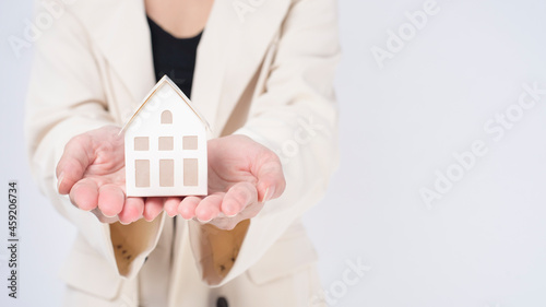 Young beautiful woman in suit holding small model house over white background studio