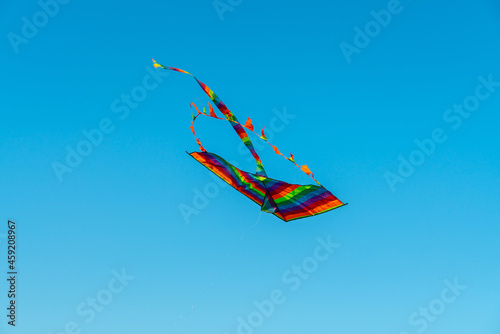 Rainbow colored kite in the clear blue skies. Selective focus.