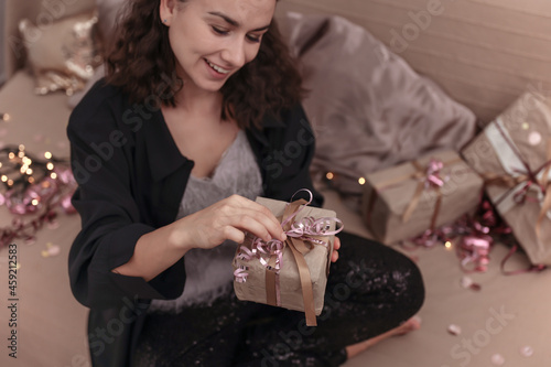 Young woman unpacks a Christmas present while sitting on the bed at home.