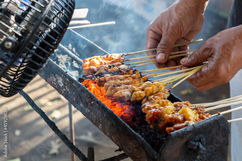 Chicken satay on traditional charcoal fire. satay on fire with smoke and an appetizing look. hands cooking satay on the grill