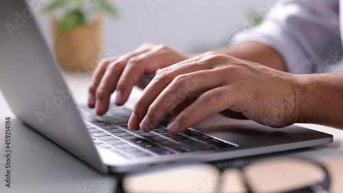 Close-up of man hands typing on laptop keyboard on white table at home office or workplace. 