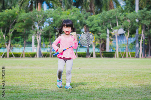 Happy child standing and holding badminton racket and shuttlecock ball. Sweet smile girl. Kindergarten kid playing sport.