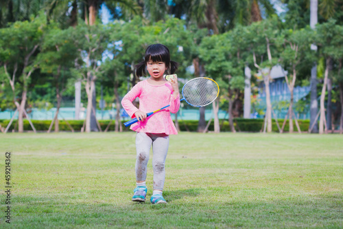 Charming little girl playing badminton in green nature park. Active child holding racket. Full body. Kid aged 4-5 years old.
