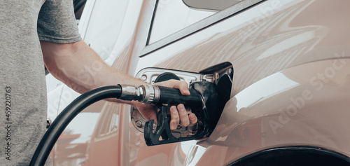 Fototapeta Closeup of man hand holds black gas pump nozzle pouring gasoline into the fuel tank of a vehicle at self service petrol station