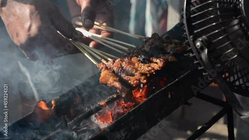 Chicken satay on traditional charcoal fire. satay on fire with smoke and an appetizing look. hands cooking satay on the grill
