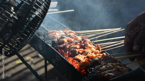 Chicken satay on traditional charcoal fire. satay on fire with smoke and an appetizing look. hands cooking satay on the grill