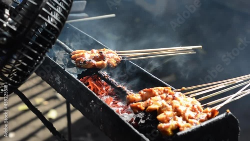 Chicken satay on traditional charcoal fire. satay on fire with smoke and an appetizing look. hands cooking satay on the grill