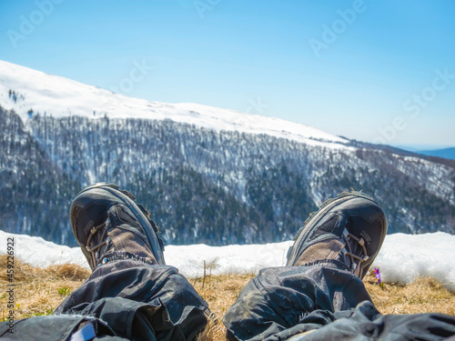 Hiker resting his feet after a long hike in the mountains.. Pair of hiking boots with Bucegi Mountains in the background. Winter landscape. photo